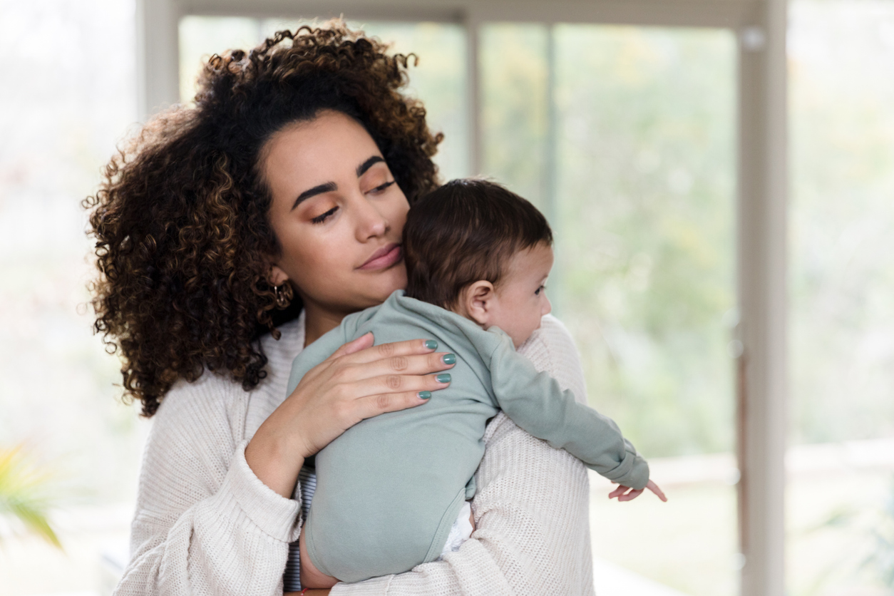 Black woman with curly hair holds baby with eyes closed