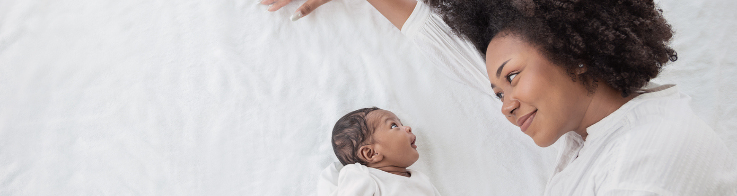Black person with curly afro smiling while laying next to newborn baby
