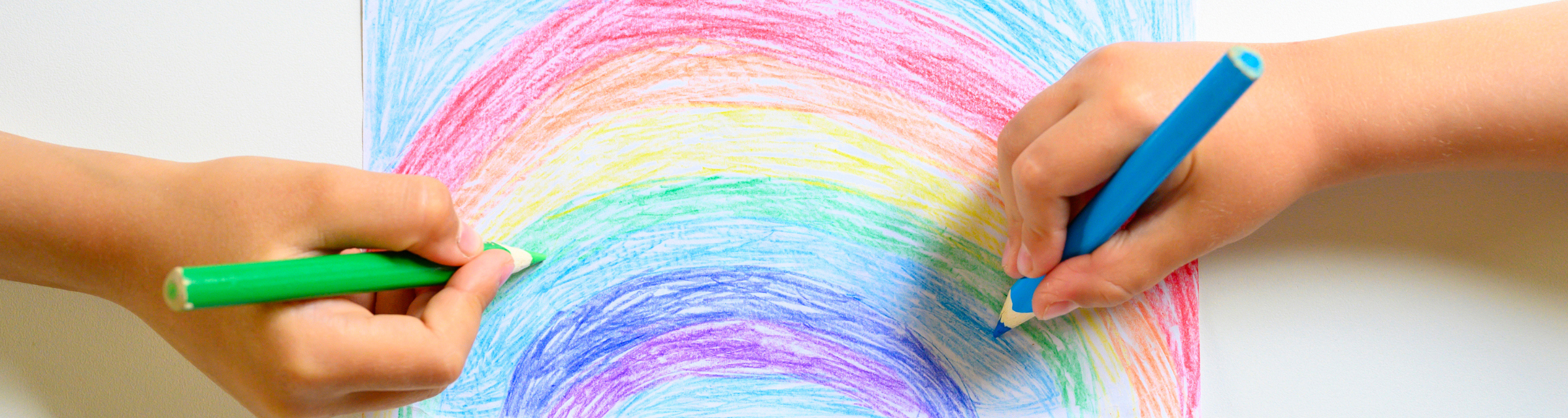 hands drawing a rainbow with crayons