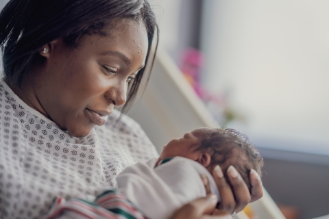 Black mother in hospital looking down at newborn baby in their hands