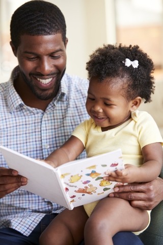 Black father reading to Black toddler with barrette in hair