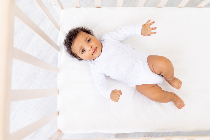 cute Black little baby with curly brown hair in white bed for sleeping