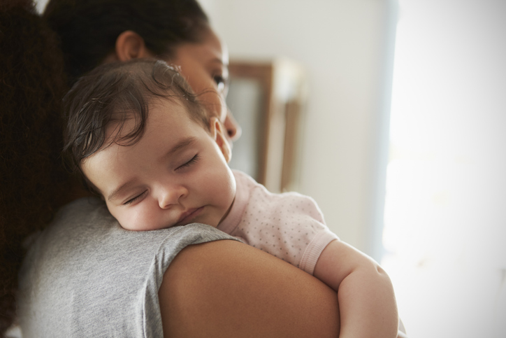 Close Up Of Mother Cuddling Sleeping Baby Daughter At Home