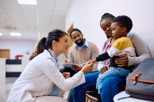 Smiling doctor holding hand on African American boy who came with parents for medical exam at pediatric clinic.