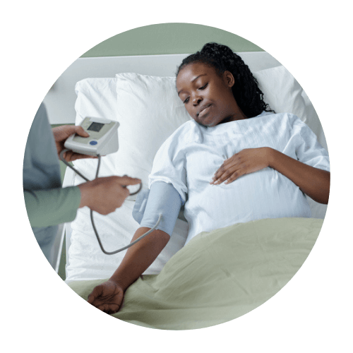 NICHQ Maternal Health Awareness Day_Image of Black pregnant person with long black hair laying in hospital bed holding her stomach and getting her blood pressure read by a nurse