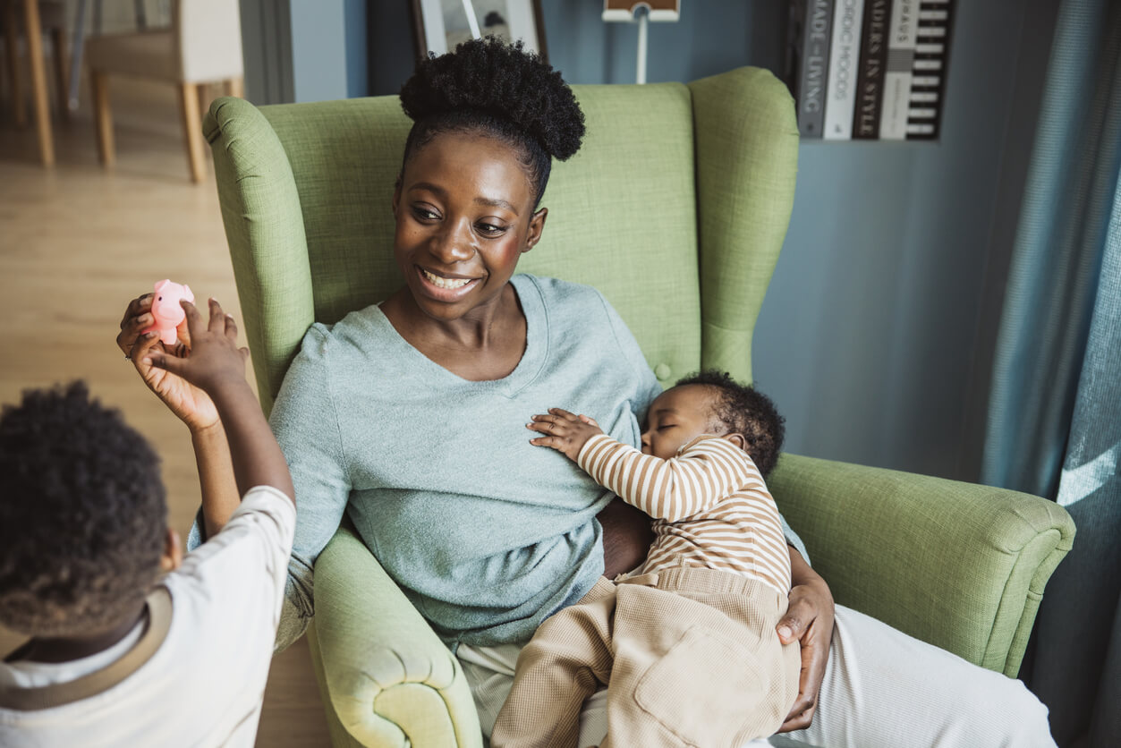 Young mother breastfeeding baby while playing with toddler.